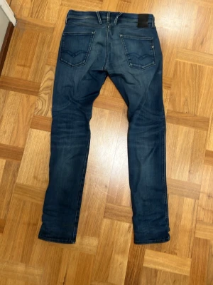 Mörkblå slim fit jeans - Snygga mörkblå slim fit jeans från replay. Jeansen har raka ben och kontrastsömmar, perfekta för en trendig vardagslook. Materialet är denim i bomull med lite stretch för extra komfort.