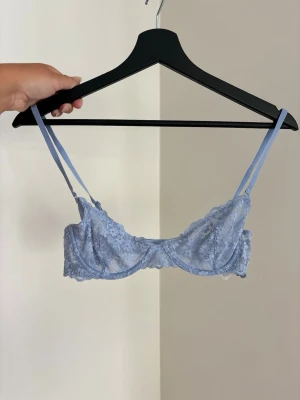 Ljusblå spets-bh med tunna band - Söt ljusblå bh i spets med blommigt mönster och tunna justerbara axelband. Bh:n har bygel och ger en feminin look med sina transparenta detaljer. Perfekt för dig som gillar romantisk och stilren underklädsel.