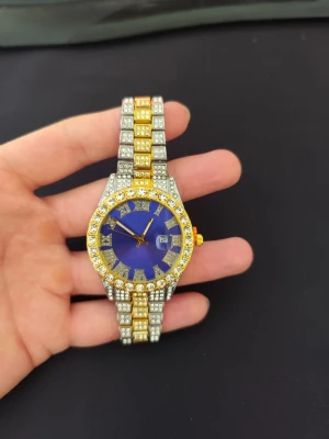 Guldig och silverfärgad klocka med blå urtavla - Snygg klocka med blå urtavla och datumvisning. Armbandet är i guld och silver med massor av glittrande stenar runt hela klockan och på länken. Perfekt för dig som gillar att sticka ut och vill ha en riktigt blingad accessoar. Minutvisaren är lite lös 
