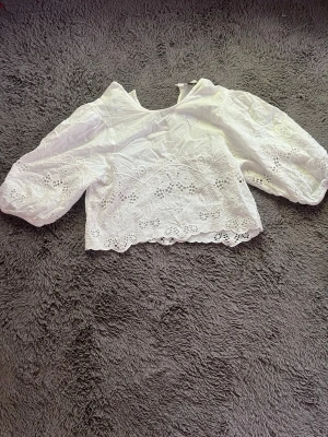 Vit broderad blus med puffärm - Söt vit blus med broderade detaljer och volangkant. Modellen är croppad med puffiga långärmar och v-ringning. Perfekt för sommarens alla tillfällen och ger en romantisk vibe till din outfit. Är i storlek L men tycker inte att den känns som en L tröja då modellen är ”puffig”. Den är från primark och nypris var runt 10 pund, säljer då den tyvärr inte används!☺️