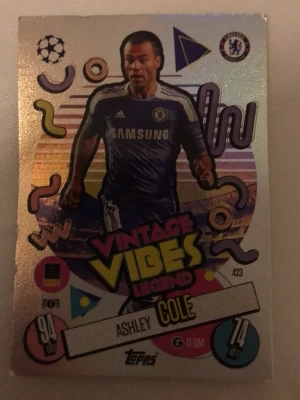Vintage Vibes Legend Ashley Cole kort - Unikt samlarkort från Topps med Ashley Cole i Chelsea-tröja. Kortet har färgglad retrodesign med texten 'Vintage Vibes Legend' och holografisk yta. Perfekt för fotbollsfans och samlare som gillar klassiska spelare.