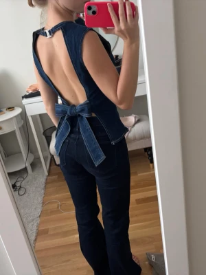 Mörkblå denim topp med öppen rygg - Säljer en snygg mörkblå denim topp med öppen rygg och stor knytrosett bak. Köpt secondhand 