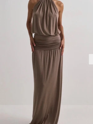 Beige set med halterneck - Säljer en elegant beige set med halterneck och draperad överdel. Det har en lös passform och är tillverkad i ett mjukt, fallande material som ger en snygg siluett. Perfekt för dig som gillar stilrena och tidlösa plagg. Setet kommer från Nelly och både överdel och underdel är i storlek M. 