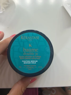 Kérastase Baume Double Je stylingbalm - Multi-talang stylingbalm från Kérastase i en rund, turkos burk med svart lock. Ger medium stadga och innehåller 75 ml. Perfekt för att forma och styla håret med en naturlig finish. (Använd 1 gång)
