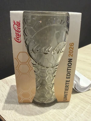 Coca-Cola McDonald's limited edition glas - Unikt Coca-Cola glas från McDonald's, limiterad upplaga 2026. Glaset har ett coolt bikakemönster och är genomskinligt med Coca-Cola-logga. Förpackningen har både McDonald's och Coca-Cola branding samt texten 'Honey'. Perfekt för samlare eller som snyggt dricksglas.