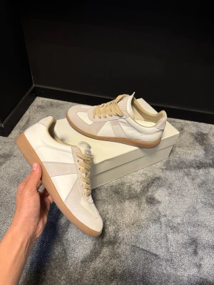 Maison margiela gats  - Stilrena sneakers i beige och vitt med klassisk design. Ovandelen är i en mix av mocka och läder, och skorna har en ljusbrun sula. Skorna är knappt använd och 100% äkta vara plus att allt og följer med. Hör av er vid funderingar och pris är diskuterbart vid snabb affär