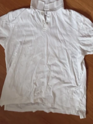 Vit polo - Klassisk vit polo med korta ärmar och knappar framtill. Tillverkad i mjukt bomullsmaterial och har en enkel, stilren design. Perfekt att matcha med jeans för en clean look.