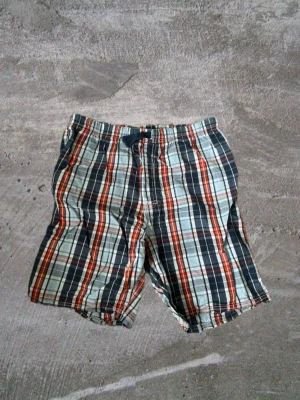 Rutiga shorts med snörning - Snygga rutiga shorts i blått, vitt och rött med elastisk midja och snörning framtill. Perfekta för sommardagar och chill häng. Lätta och sköna med avslappnad passform.