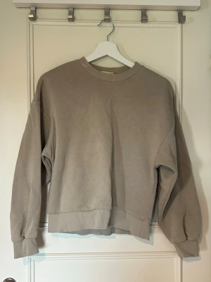 Beige sweatshirt - En beige sweatshirt med rund halsringning och ribbade muddar vid ärmslut och nederkant från Gina Tricot i stl XS. Missfärgning vid halsringning annars fint skick.