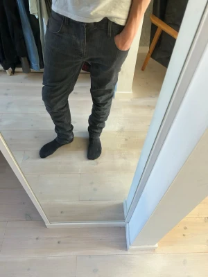 Mörkgrå herr jeans med cool tvätt! - Säljer ett par mörkgrå slim fit jeans med klassisk femficksmodell och dragkedjegylf. Jeansen har en smal passform och är tillverkade i ett mjukt denimtyg som ger en bekväm känsla. Perfekta för dig som gillar en stilren och enkel look.