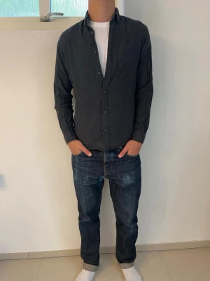 Mörkgrå skjorta från Essentials - Säljer en stilren mörkgrå skjorta i 100% bomull från Essentials av Jack and Jones med klassisk krage och knäppning framtill. Skjortan har lång ärm och en bröstficka, perfekt för en avslappnad men ändå lite uppklädd look. Passar riktigt bra till jeans en kyligare höstdag. Storlek S men passar även M. Hör av dig vid frågor!🙌
