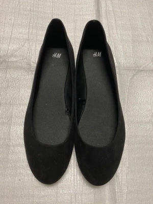 Svarta ballerinaskor från H&M - Klassiska svarta ballerinaskor från H&M med rund tå och enkel design. 