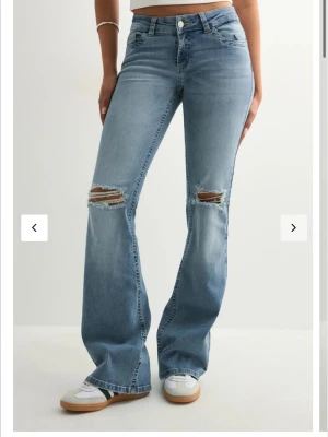 Bootcut ljusblå jeans med hål  - Säljer ett par ljusblå bootcut jeans med hål på   knäna. Jeansen har klassisk femficksmodell  och är tillverkade i denim med lite stretch. Köpte dem på Nelly för 699kr