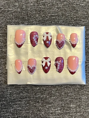 Press-on naglar || storlek S - Snygga press-on naglar i mandelform med rosa och vinröda toner storlek S. Dekorerade med vita pärlor, glitter och 3D-rosetter för en extra söt look. Några naglar har glittriga detaljer och andra har pärlkanter. Perfekt för dig som vill ha unika och glamorösa naglar för alla hjärtans dag🌺 Det du får med dig : * Fil och manikyr pinne * nagellim klistermärken * 2 lappar av rengöring för naglar.