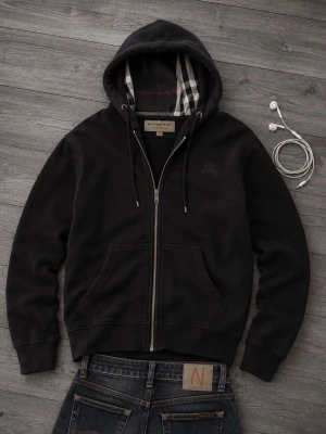Svart hoodie med dragkedja Burberry - Snygg svart hoodie från Burberry med dragkedja framtill och klassiskt rutigt foder i huvan. Hoodien har långa ärmar, snörning i huvan och två fickor fram. Perfekt för en avslappnad och stilren look.