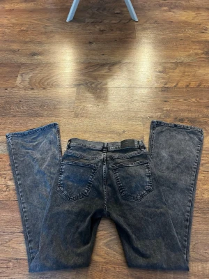Svarta raka jeans med tvättad look - Säljer ett par mörk grå jeans med tvättad vintage-look och raka ben. Jeansen har klassisk femficksmodell, bälteshällor och knappgylf. Perfekta för en avslappnad och trendig stil.