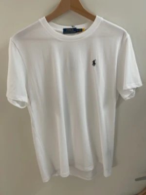 Vit t-shirt från Polo Ralph Lauren - Klassisk vit t-shirt från Polo Ralph Lauren med den ikoniska lilla loggan broderad på bröstet. T-shirten har rund hals, korta ärmar och är gjord i mjuk bomull för en skön och clean look.