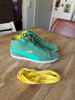 Gröna Puma sneakers med gula detaljer - Snygga gröna sneakers från Puma i mocka med turkos sidostrip och gula detaljer. Skorna är mellanhöga och har gula innersulor samt extra gula skosnören. Perfekta för dig som vill sticka ut med färg och stil.