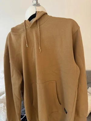 Beige hoodie från Jack & Jones - Snygg beige hoodie från Jack & Jones med klassisk känguruficka och dragsko i huvan. Tillverkad i mjukt bomullsmaterial som känns skönt mot huden. Perfekt för en avslappnad och trendig look.