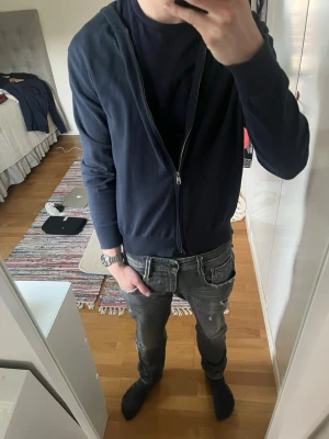 Mörkblå hoodie med dragkedja - Snygg mörkblå hoodie med dragkedja framtill och huva. Tillverkad i ett mjukt och tunt material som känns skönt mot huden. Modellen har långa ärmar och ribbade muddar vid ärmslut och nederkant. Perfekt att slänga på sig över en t-shirt.