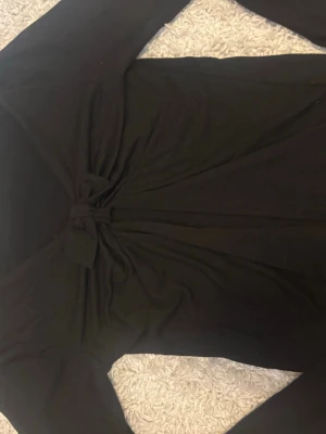 Svart långärmad topp med knut - Säljer en svart långärmad topp från H&M med snygg knutdetalj framtill. Toppen har en enkel och stilren design som passar till många olika looks. Materialet känns mjukt och stretchigt, perfekt för dig som gillar bekväma plagg.