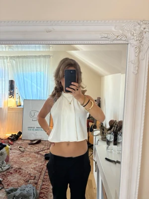 Vit ärmlös croppad linnetopp - Snygg vit croppad linnetopp med hög hals och lös passform. Toppen är ärmlös och har en stilren, enkel design som passar perfekt till både jeans och kjol. Materialet känns lätt och luftigt, perfekt för varmare dagar.