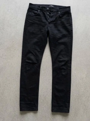 Svarta slim fit jeans från Neuw - Säljer ett par svarta slim fit jeans från Neuw med knappgylf . Jeansen har raka ben och är tillverkade i ett denimtyg som sitter snyggt. Perfekta för dig som gillar en clean och stilren look. Storlek 29:30