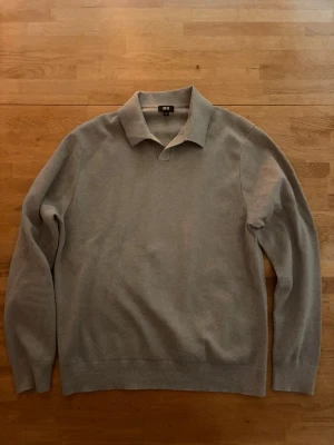 Uniqlo Tröja - En stilren grå stickad tröja från Uniqlo med klassisk krage och långa ärmar. Tröjan har en mjuk och tunn stickning som gör den perfektion för lager på lager. Enkel design utan mönster och ribbade muddar vid ärmslut och nederkant. Otroligt bra skick. Endast använd två gånger.