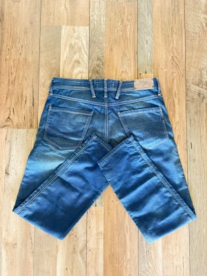 Blå jeans från Replay - Snygga blå jeans från Replay med klassisk femficksmodell och raka ben. Jeansen har tydliga kontrastsömmar och en läderpatch med Replay-logga bak i midjan. Perfekta för en avslappnad och trendig stil.