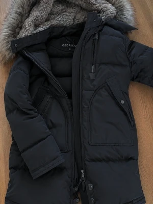 Cedrico jacka  - Snygg svart dunjacka från Cedrico med avtagbar huva och päls. Jackan har två stora snedställda fickor med lock, dragkedja och knappar framtill samt mjukt foder i huvan. Perfekt för kalla vinterdagar. Jackan är i superfint skick och köpt på johnells förra vintern. Ny pris: 8499kr. Jacka är i storlek xs men passar även en s. Går att hämta upp i norrköping om man skulle vilja det. Annars kan jag posta den.