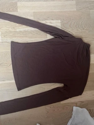 Brun långärmad topp - En enkel och stilren brun långärmad topp i mjukt material. Perfekt att matcha med jeans eller kjol för en clean look. Modellen är rak och har en klassisk passform utan synliga detaljer eller mönster.