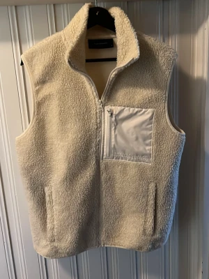 Beige teddyväst peackperformance - Mysig beige teddyväst från peakperformance i fleece med hög krage och dragkedja framtill. Västen har en bröstficka med dragkedja och två sidofickor. Perfekt för lager-på-lager och ger en avslappnad look.