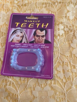 Blåa vampyrtänder för maskerad - Säljer ett par blåa vampyrtänder i plast, perfekta för maskerad eller cosplay. Tänderna är mjuka och flexibla, enkla att använda och passar de flesta. Förpackningen har bilder på klassiska skräckkaraktärer och texten MAKEUP TEETH.
