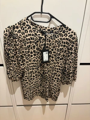 Leopardmönstrad topp med puffärm - Snygg topp med leopardmönster i beige och svart. Modellen har puffärmar och rund halsringning. Materialet känns mjukt och stretchigt, perfekt för att lyfta vilken outfit som helst. Stängs inte med knappar eller dragkedja. Helt ny, nypris 150kr
