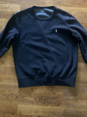 Svart sweatshirt från Polo Ralph Lauren - Klassisk svart sweatshirt från Polo Ralph Lauren med rund halsringning och broderad logga på bröstet. Tröjan har ribbade muddar vid ärmslut och nederkant samt en avslappnad passform. Perfekt till jeans eller chinos.