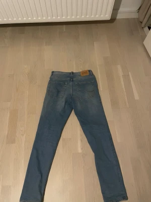 Blå slim fit jeans med skinnpatch - Snygga blå slim fit jeans med klassisk femficksdesign och en brun skinnpatch bak i midjan. Jeansen har raka ben och är tillverkade i ett mjukt denimtyg som ger en bekväm känsla. Perfekta för en avslappnad och trendig look. Skick 9/10 knappast använda.