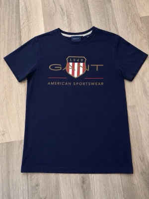 Marinblå GANT t-shirt med tryck - GANT T-shirt 💙  Säljer en snygg GANT T-shirt i bra skick. • Storlek: [xs] • Färg: [mörk blå] • Märke: GANT • Pris: 200 kr • Skick: [mycket bra]  Perfekt till vardags och passar enkelt med jeans eller shorts 👕 Skickas snabbt och packas noggrant 📦