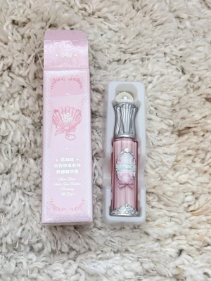 Flower knows Rosa läppglans med pärldetaljer - Supersött läppglans i ljusrosa nyans med elegant silverfärgat lock och pärldetalj på toppen. Förpackningen har en vintageinspirerad design med dekorativa mönster och en liten rosett på etiketten. Perfekt för dig som älskar gulliga och unika sminkprodukter.