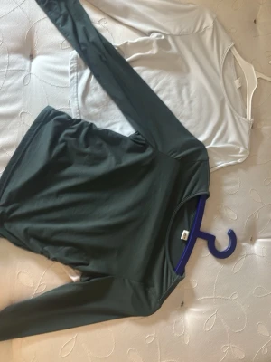 Två långärmade toppar i grönt och vitt - Säljer två basic långärmade toppar, en i grönt och en i vitt. Båda har rund halsringning och är tillverkade i mjukt material som känns skönt mot huden. Perfekta att matcha med jeans eller kjol för en enkel och clean look.