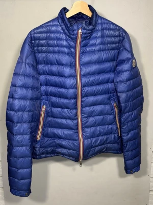 Daniel Down Jacket - Dunjacka från Moncler i en sällsynt blå färg. Jackan är i fint skick med endast en liten lagning (se bild 5), vilket inte är något man tänker på vid användning. Storlek 3 sitter som en M.