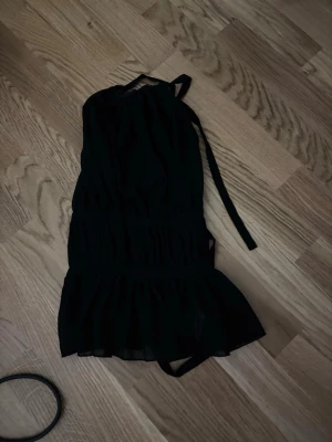 Svart halterneck topp med volang - Säljer en svart halterneck topp med knyt i nacken och volang nedtill. Toppen har en luftig passform och är perfekt för dig som gillar en stilren men ändå trendig look. Materialet känns lätt och flowy, vilket gör den skön att bära.