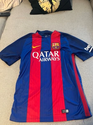 FC Barcelona matchtröja Nike storlek S/M  - Säljer en FC Barcelona matchtröja från Nike i storlek M. Tröjan är blå och röd med klubbmärke, Qatar Airways-tryck och Dri-FIT-material som andas. Korta ärmar och klassisk passform, perfekt för fotboll eller träning.