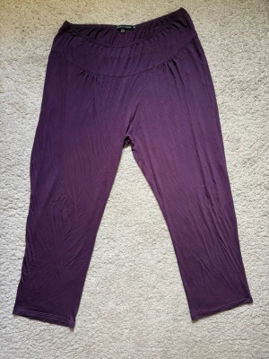 Lila byxor från Gudrun Sjödén, stl XL -NYA! - Helt nya och oanvända, endast upptvättade. Bekväma och mjuka byxor i färgen aubergine, varm mörklila.från Gudrun Sjödén i storlek XL. Byxorna har en bred, elastisk midja med diskret spetskant, perfekta för både vardag och avslappning. Materialet är tunt och följsamt, vilket gör dem sköna att bära. Absolut nyskick!