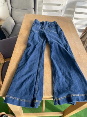 Blåa utsvängda jeans - Säljer ett par blåa jeans med utsvängda ben och kontrastsömmar. Klassisk femficksmodell i mjukt denimtyg. Perfekta för dig som gillar retrostil och vill ha ett par riktigt snygga jeans med bred passform. Använda 2 gånger 
