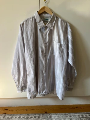 Randig skjorta strl 45/46 - Säljer en skjorta med ljusgrå och vita ränder. Skjortan har klassisk krage, bröstficka och knappar framtill. Storlek 45/46