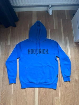 Hoodrich hoodie  - Snygg blå hoodie från HOODRICH med stor svart logga på bröstet. Hoodien har huva med dragsko, magficka och ribbade muddar vid ärmar och nederkant. Perfekt för en chill och streetwear-inspirerad look.