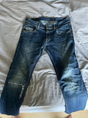 Mörkblå tiger jeans med slitningar - Säljer ett par blå tiger jeans med tydliga slitningar och distressed detaljer på knäna. Jeansen har fem fickor, normal midja och raka ben. Materialet är klassisk denim i bomull och färgen är tvättad blå med ljusare partier. Perfekt för festklädsel mm. Dem är i storlek w31 men sitter mer som 30-29 i midjan, skriv gärna vid funderingar👍