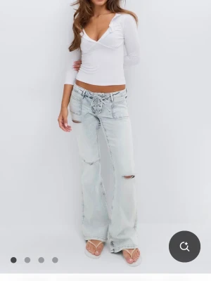 Ljusblå flare jeans  - Säljer ett par ljusblå jeans som är utsvängda flare/bootcut med slitningar vid knäna. Jeansen har en snygg knytdetalj i midjan. Klassisk femficksmodell i denim som ger en avslappnad och trendig look. Använd ett fåtal gånger (bra skick)