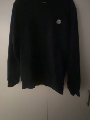 Svart tröja från Moncler - Svart tröja från Moncler med rund halsringning och Moncler-logga broderad på bröstet. Tröjan har lång ärm och en klassisk, enkel design som passar till det mesta. Perfekt för dig som gillar stilrena plagg med exklusiv känsla.
