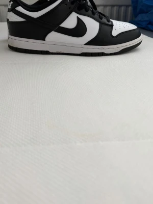 Nike Dunk Low svart/vit sneaker - Säljer ett par Nike Dunk Low sneakers i svart och vitt. Skorna har klassisk låg siluett, svart swoosh och ovandel i läder. Yttersulan är svart och mellansulan vit. Perfekta för dig som gillar stilrena och tidlösa sneakers.